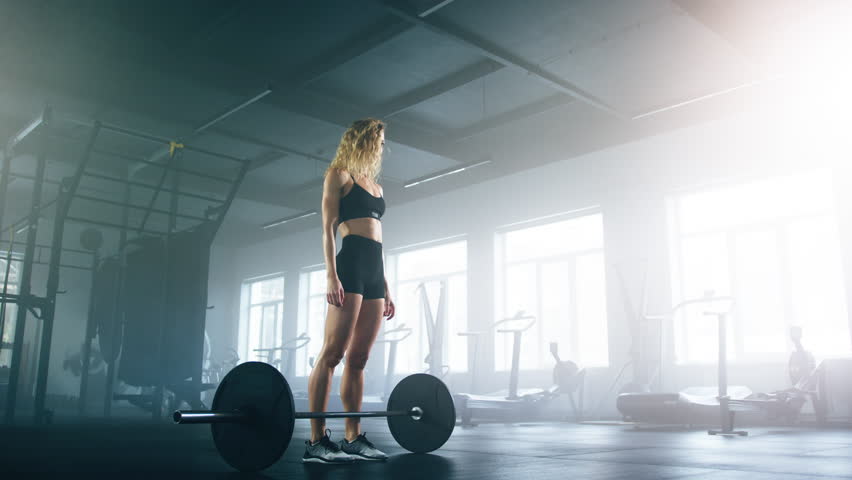 Close-up view of female athlete using a barbell during a powerlifting workout. Portrait of a CrossFit sportswoman performing deadlift exercise in gym studio. High quality 4k footage
