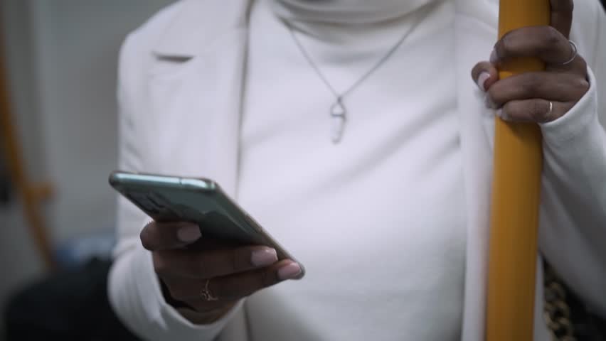 Pretty young African girl standing using cell phone in subway. Beautiful happy black woman consulting phone on transport. Cosmopolitan people moving around the city.  | Shutterstock HD Video #1100349165