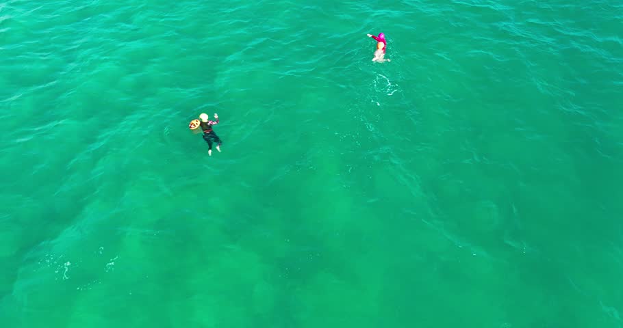top view Two people swimming in shallow in sunny day, the ocean is calm and peaceful, full view of people realxing on beach from high angle shot.
