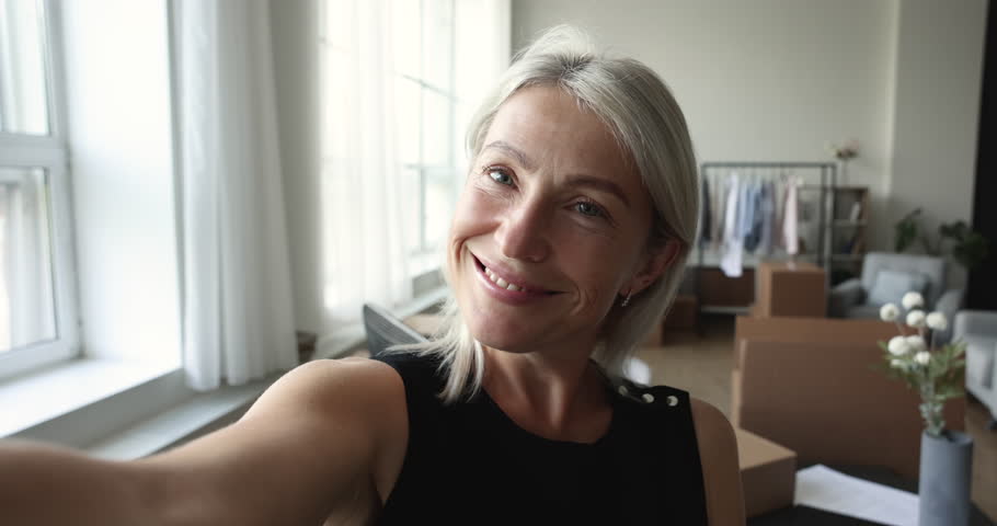 Close up mature woman record video for vlog, boasts with relocation, moving day at new home, boxes with stuff stacked in living room. Video call, entrepreneur start own business at new rented office Royalty-Free Stock Footage #1100353661