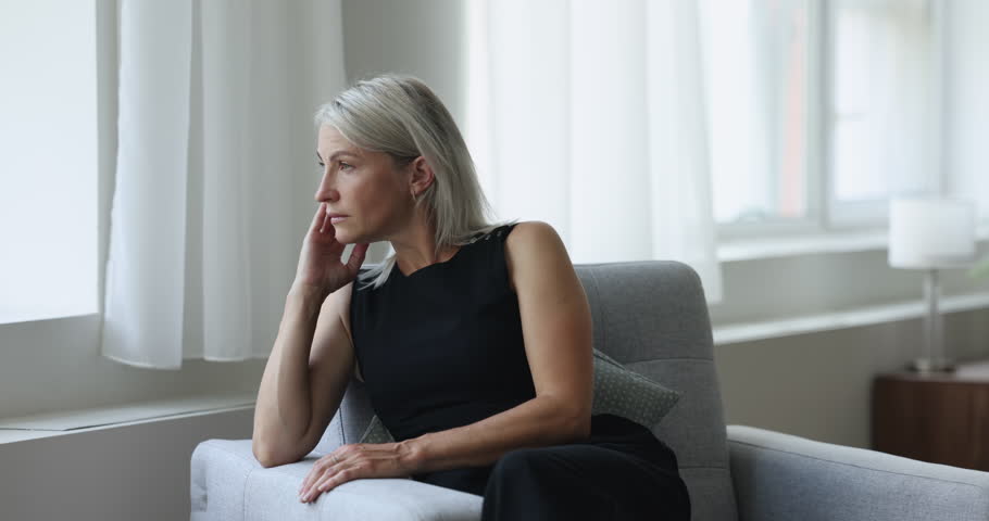 Middle age thoughtful, pensive woman sits on armchair staring out of window, ponders, thinking, missing or waiting, looks frustrated, recall life and recollects memories, resting alone in living room Royalty-Free Stock Footage #1100353669