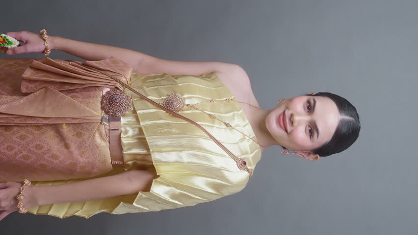 Vertical video. A young asian woman wearing Thai traditional cloth on gray background