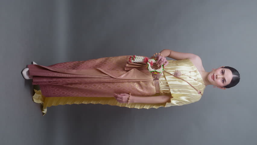 Vertical video. A young asian woman wearing Thai traditional cloth on gray background