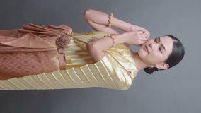 Vertical video. A young asian woman wearing Thai traditional cloth on gray background