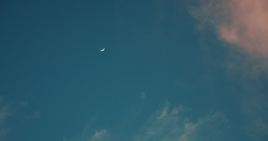 Moon on blue sky with fluffy pink clouds.