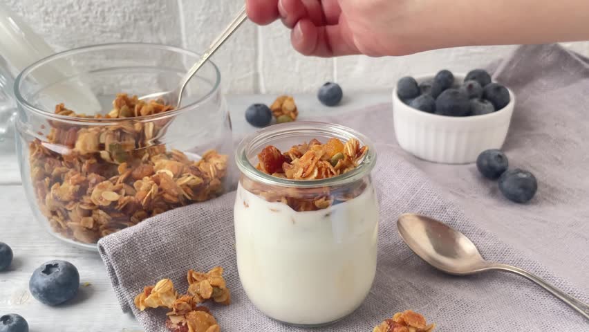Yogurt with muesly granola and blueberries. Spoon with granola filling the jar. Royalty-Free Stock Footage #1100369947