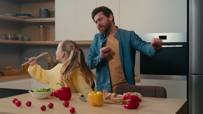 Funny Caucasian bearded father dancing moving funny dance while little kid daughter child girl singing song in spoon like microphone sing karaoke in kitchen family having party fun cooking together Royalty-Free Stock Footage #1100371201