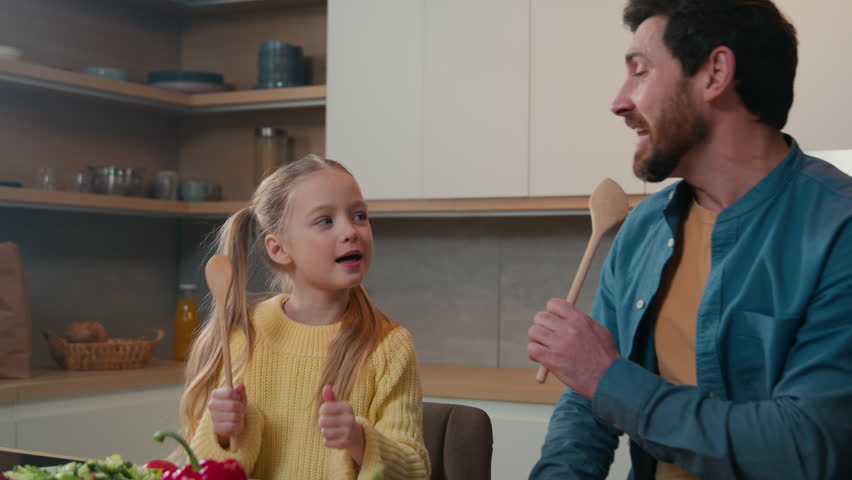 Funny Caucasian bearded father and cute little kid daughter singing song in kitchen funny cooking happy family dad with child girl holding spoon use like microphone sing enjoy cook having fun together Royalty-Free Stock Footage #1100371203