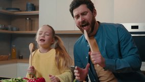 Funny Caucasian bearded father and cute little kid daughter singing song in kitchen funny cooking happy family dad with child girl holding spoon use like microphone sing enjoy cook having fun together - Powered by Shutterstock - Get 15% off with code: PIKWIZARD15