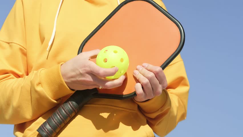 hands female player pickleball game with paddle and pickleball yellow ball, outdoor sport leisure activity