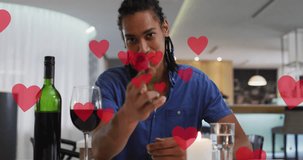 Animation of hearts over biracial man drinking wine and having video call. Valentines day and celebration concept digitally generated video.