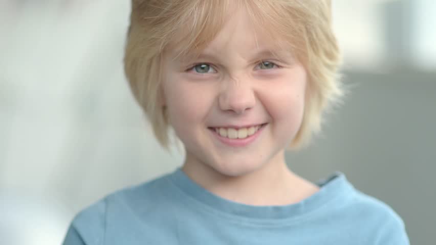 Slow motion close-up portrait of happy school-age child. Cute boy with blond hair emotionally laughs and looks at you. Real emotions of kids. Beautiful european child smiles and rejoices Royalty-Free Stock Footage #1100379889
