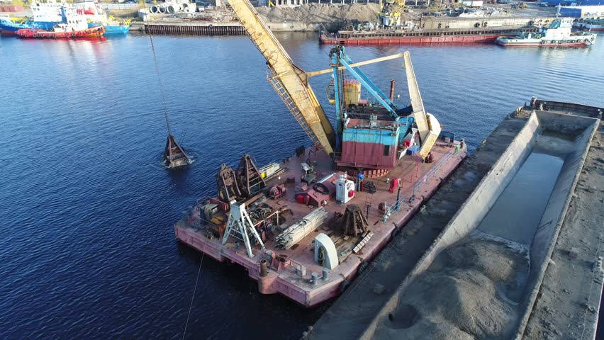 Aerial view. The dredger is working. Extraction of river sand by a special floating crane. A dredging machine takes sand from the bottom of the river and loads it onto a barge.   Royalty-Free Stock Footage #1100380493