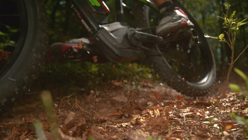 CLOSE UP, SLOW MOTION, LOW ANGLE: Dry brown leaves fly up in the air as the unrecognizable male downhill cyclist rides through the forest. Cinematic shot of a man riding electric bike in the woods. Royalty-Free Stock Footage #1100380691