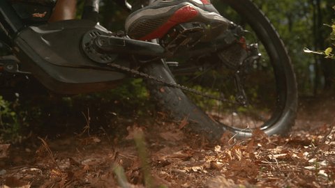 CLOSE UP, SLOW MOTION, LOW ANGLE: Dry brown leaves fly up in the air as the unrecognizable male downhill cyclist rides through the forest. Cinematic shot of a man riding electric bike in the woods. Vídeo Stock