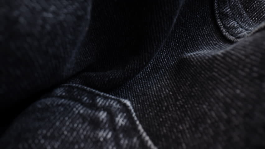 Macro shot black denim jeans material. Slider dolly extreme close-up of clothing material, camera glides over fabric texture. Seams sewn with black threads. Shot with laowa 24mm lens Royalty-Free Stock Footage #1100381709