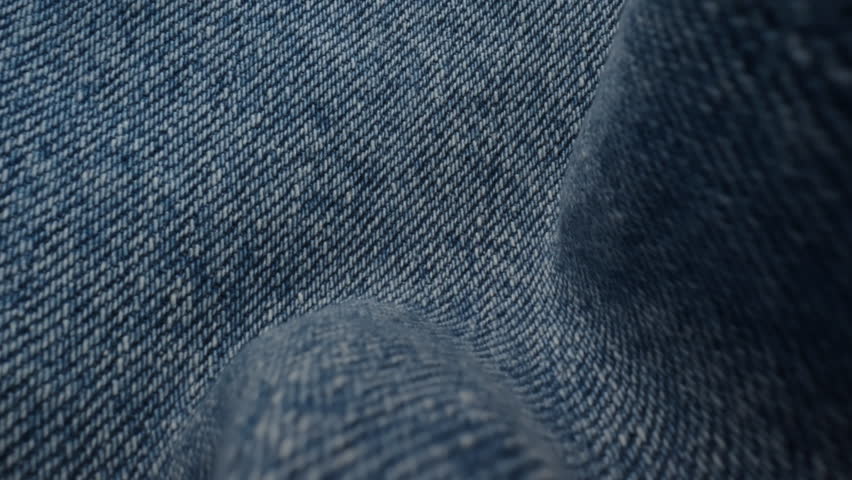 Macro shot blue denim jeans material. Slider dolly extreme close-up of clothing material, camera glides over fabric texture. Seams sewn with yellow threads. Shot with laowa 24mm lens
