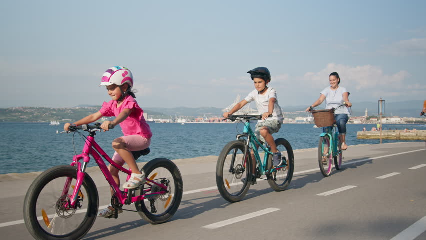 Caucasian mother, father, and two children having fun on vacation cycling near the sea, tracking shot. Family coastal bike ride. Royalty-Free Stock Footage #1100382785