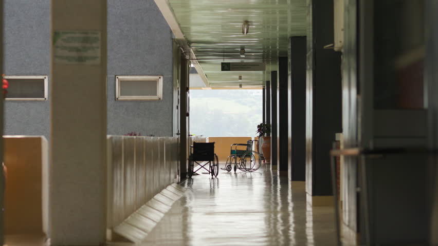 employee pushing empty cart away from camera with two empty wheel chairs at end of hallway in Rwandan Hospital.