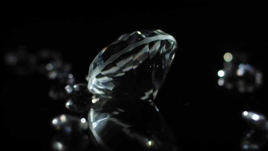 A slow turning sparkling diamond on a dark shiny surface to indicate luxury or wealth or as a gift for special occations like weddings valentines day.