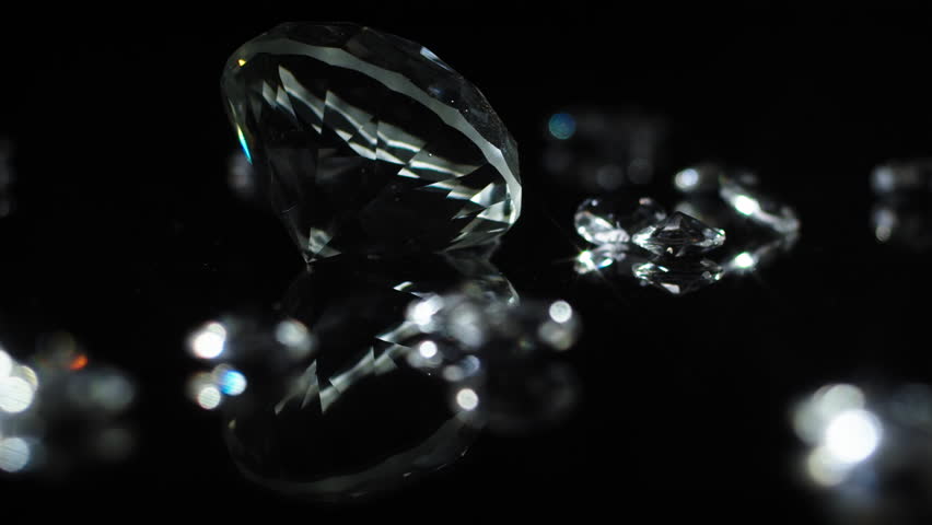 Slow turning large cristal clear diamond with smaller shiny diamonds on a dark mirroring surface to indicate luxury or wealth or as a gift for special occations like weddings or valentines day.