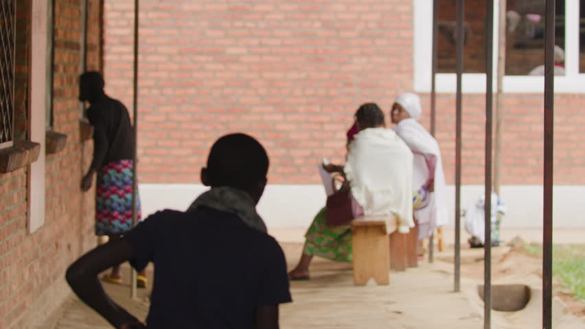 Boy walks away from camera with people sitting in the background of hospital hallway in Rwanda.