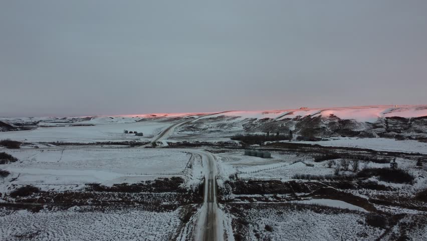 Aerial view along an old gravel road in a badlands coulee at Sharples, Alberta as the morning sun lights up the hills above the valley walls.