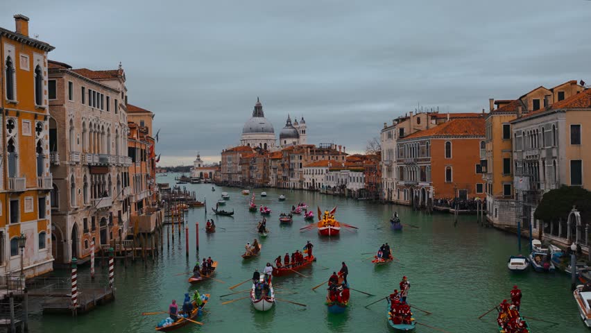 Venice Carnival 2023 at Canale Grande, Grand Canal, close to Rialto Bridge. Celebration with colorful rowing boats in the old Italian city. Venetian masks and costumed people in Saint Mark