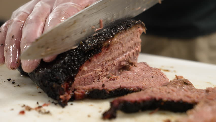Pitmaster carefully slices tender Texas smoked barbecue beef brisket for plating, slow motion close up 4K