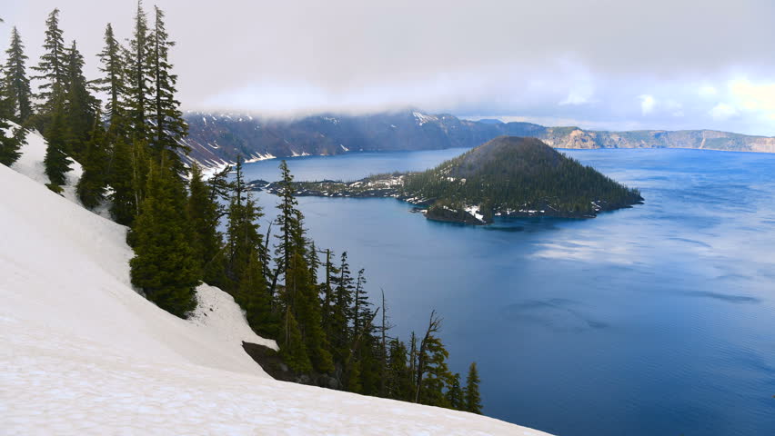 Spring at Crater Lake - A time-lapse video of foggy low clouds flying over blue Crater Lake and rocky Wizard Island on a stormy Spring evening. Crater Lake National Park, Oregon, USA.