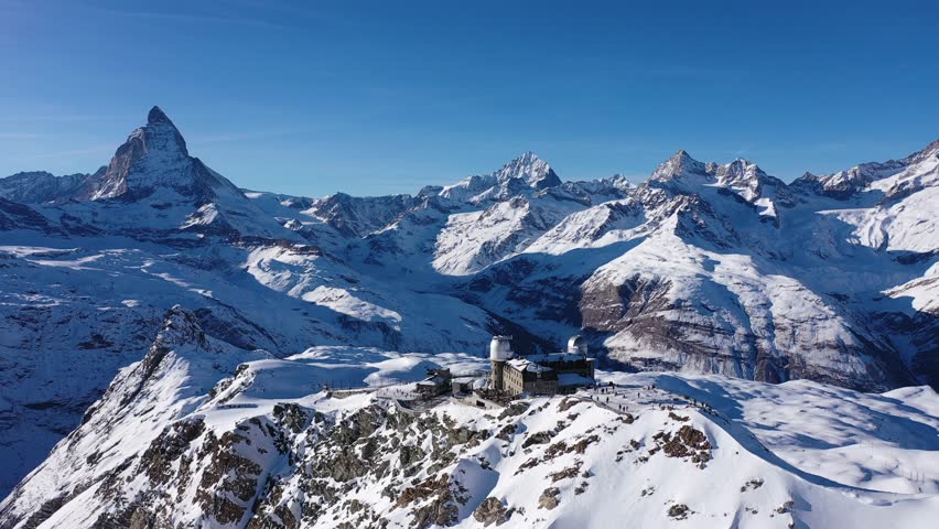 Scenic aerial view of mountain ridge Gornergrat in Pennine Alps covered with snow with building of hotel, observatory and rack railway station on background of Matterhorn peak, Zermatt, Switzerland