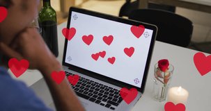 Animation of hearts over biracial man drinking wine and using laptop with copy space. Valentines day and celebration concept digitally generated video.