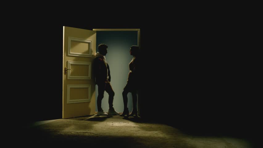 Side view of couple standing opposite and looking each other in front of an open door with galaxy behind . Footage of couple stand on floor behind stars.  Concept of dream or romance . Slow Motion