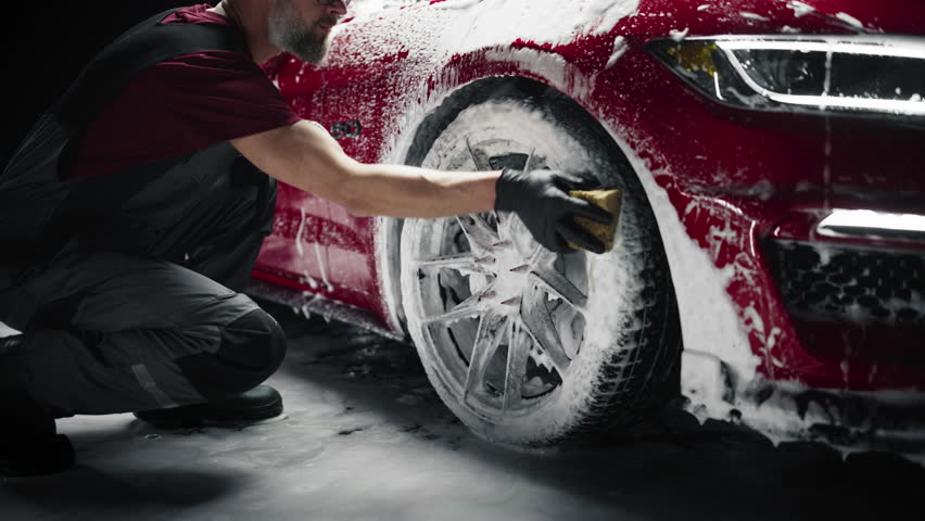 Car Ad Style Footage of a Professional Car Wash Specialist Using a Big Soft Sponge to Wash the Rims of a Beautiful Red Sportscar with Shampoo Before Detailing, Polishing and Waxing Royalty-Free Stock Footage #1100395805