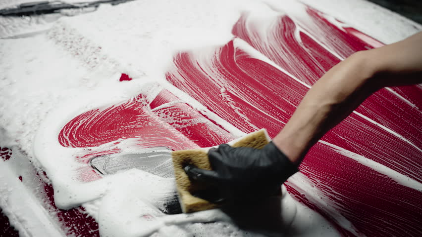 Car Ad Style Footage of a Professional Car Wash Specialist Using a Big Soft Sponge to Wash a Beautiful Red Sportscar with Shampoo Before Detailing, Polishing and Waxing
