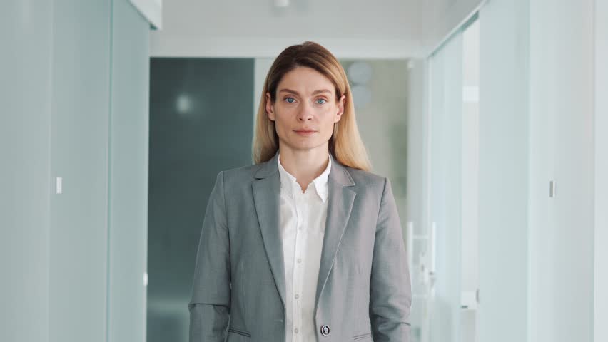 Concentrated focused young female professional financial, advisor, leader boss CEO manager looking seriously to camera. Young girl office worker standing in loft modern glass office hall.  | Shutterstock HD Video #1100398107