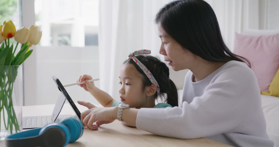 Cute asia people alpha small Gen Z kid fun talk play learn on smart tablet app game with mum at home sofa. Enjoy Child care little girl and mom happy smile relax teach study upskill idea online class.