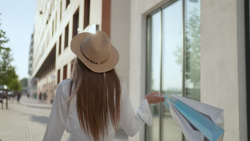 Young tourist happy attractive smiling woman in hat walking with colorful shopping bags around shopping mall at sunset summer city street. Shopping girl walking outdoors. Black friday. Travel tourism | Shutterstock HD Video #1100402069