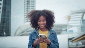 Happy young African American woman walking down the city street smiling using mobile phone chatting online with friends, Female in jean jacket walks down the street using social media on smartphone - Powered by Shutterstock - Get 15% off with code: PIKWIZARD15