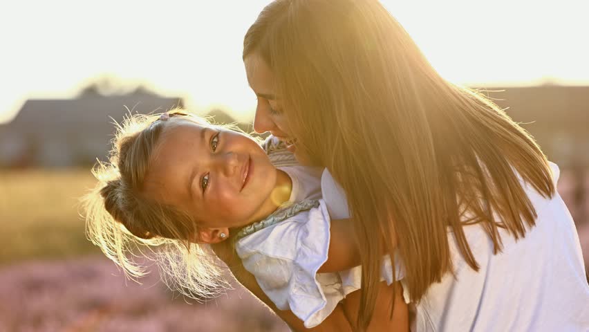 family day. young mom and little daughter enjoy relaxing in a field with lavender at sunset. A beautiful mother hugs and kiss child girl tightly. Maternal care and love for the child. mothers day. Royalty-Free Stock Footage #1100404959