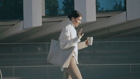 Busy trendy businesswoman talking through wireless headphones walking city street. Stylish confident business lady holding cup coffee takeaway going to office. Young woman calling using modern headset - Powered by Shutterstock - Get 15% off with code: PIKWIZARD15