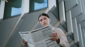 Serious young woman reading newspaper on city street close up. Attractive confident business lady deploying periodical press standing in front modern office building. Elegant girl looking media news. - Powered by Shutterstock - Get 15% off with code: PIKWIZARD15