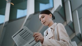 Young confident business woman holding newspaper standing in front modern office building close up. Elegant successful lady reading financial article outdoors on city street. Press publication concept - Powered by Shutterstock - Get 15% off with code: PIKWIZARD15