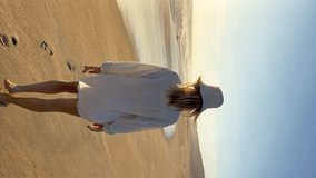 young woman in casual linen clothes walking on the beach alone at sunset in Mexico