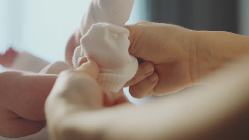 Closeup of a young mother putting warm socks on her baby legs while lying on the bed. Shot in slow-motion Royalty-Free Stock Footage #1100407399