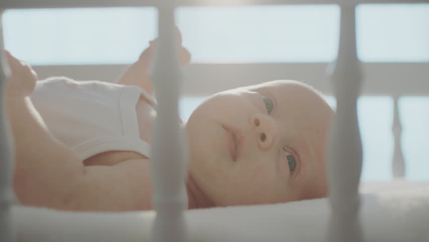 Mother kssing kid's cheek and baby crying at wooden cradle against large window with bright light close-up. Shot in slow-motion Royalty-Free Stock Footage #1100407509