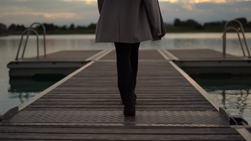 Back view of woman with braids walking on platform, lake, sunset time