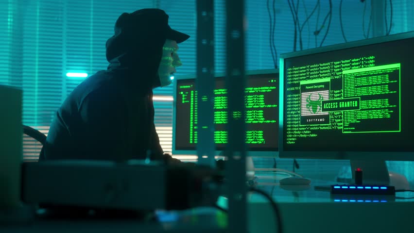 Hacker in a white mask is typing on a computer keyboard and cracking a password. Access denied, access granted. A man in a black hoodie and gloves. The mask reflects green symbols of program codes. Royalty-Free Stock Footage #1100412733
