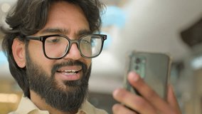 30s Indian bearded guy talk video call conversation on smart phone. Modern wireless technology usage. Arabian man in eyeglasses businessman talking to mobile web camera remote communication conference
