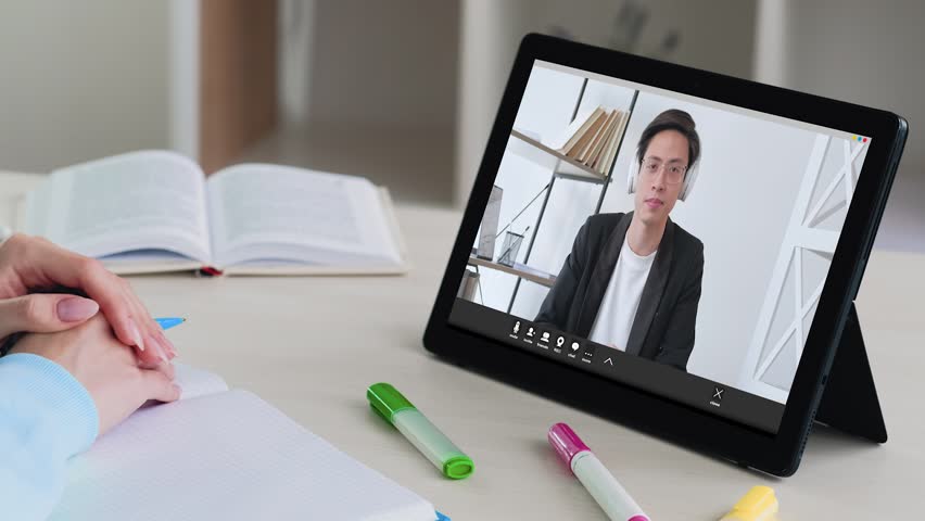 Business webinar. Video presentation. Online conference. Confident male coach in headphones introducing statistics report to female student on tablet at modern workplace.